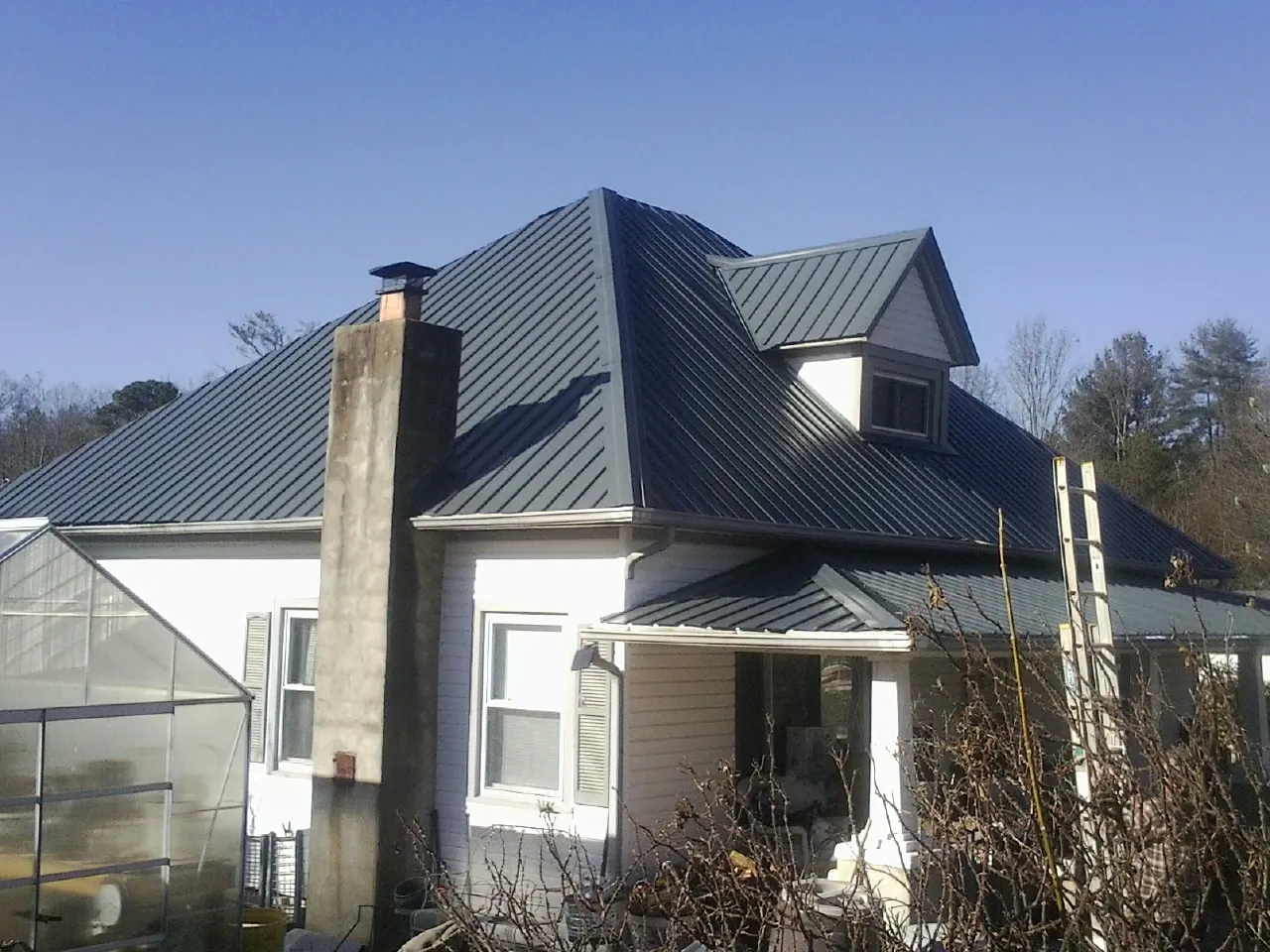 Dark blue standing seam metal roof on a white farmhouse with dormer — Slate & Tile Roof Repair by Roofing Brothers in Mystic