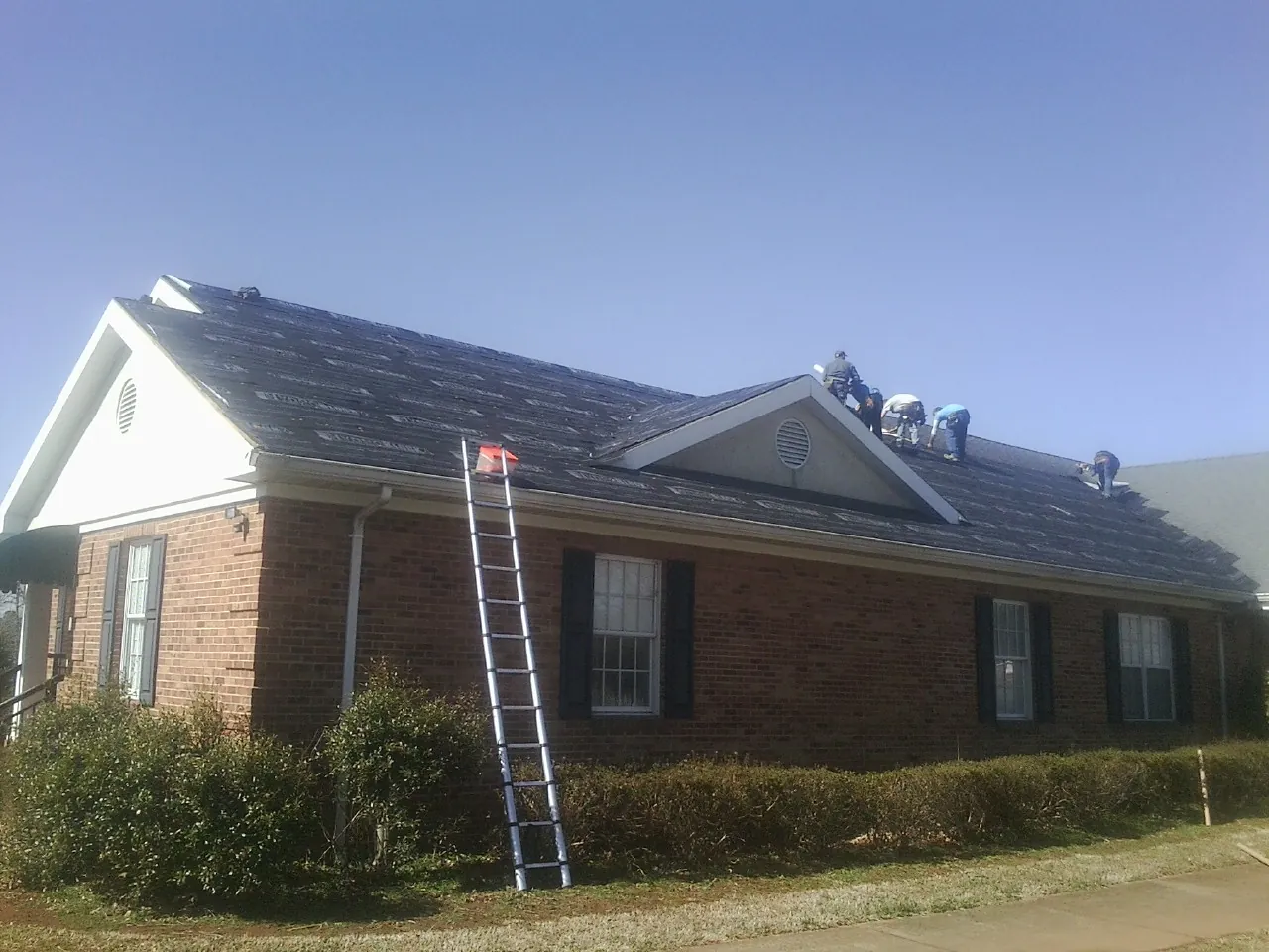 Crew tearing shingles off a brick ranch roof with a ladder set — Metal Roof Repair work by our crew in Mystic