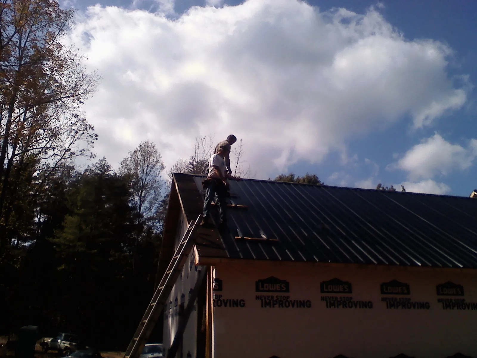 Roofer fastening dark metal panels high against a cloudy sky, from a Roof Inspection job in Mystic