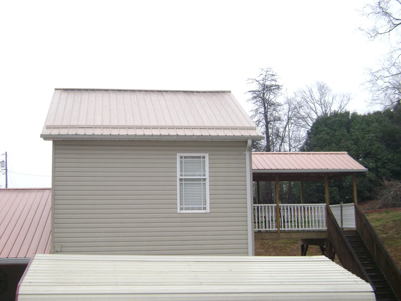 Tan metal roofs on a two story addition and attached porch, from a Roof Replacement job in Mystic